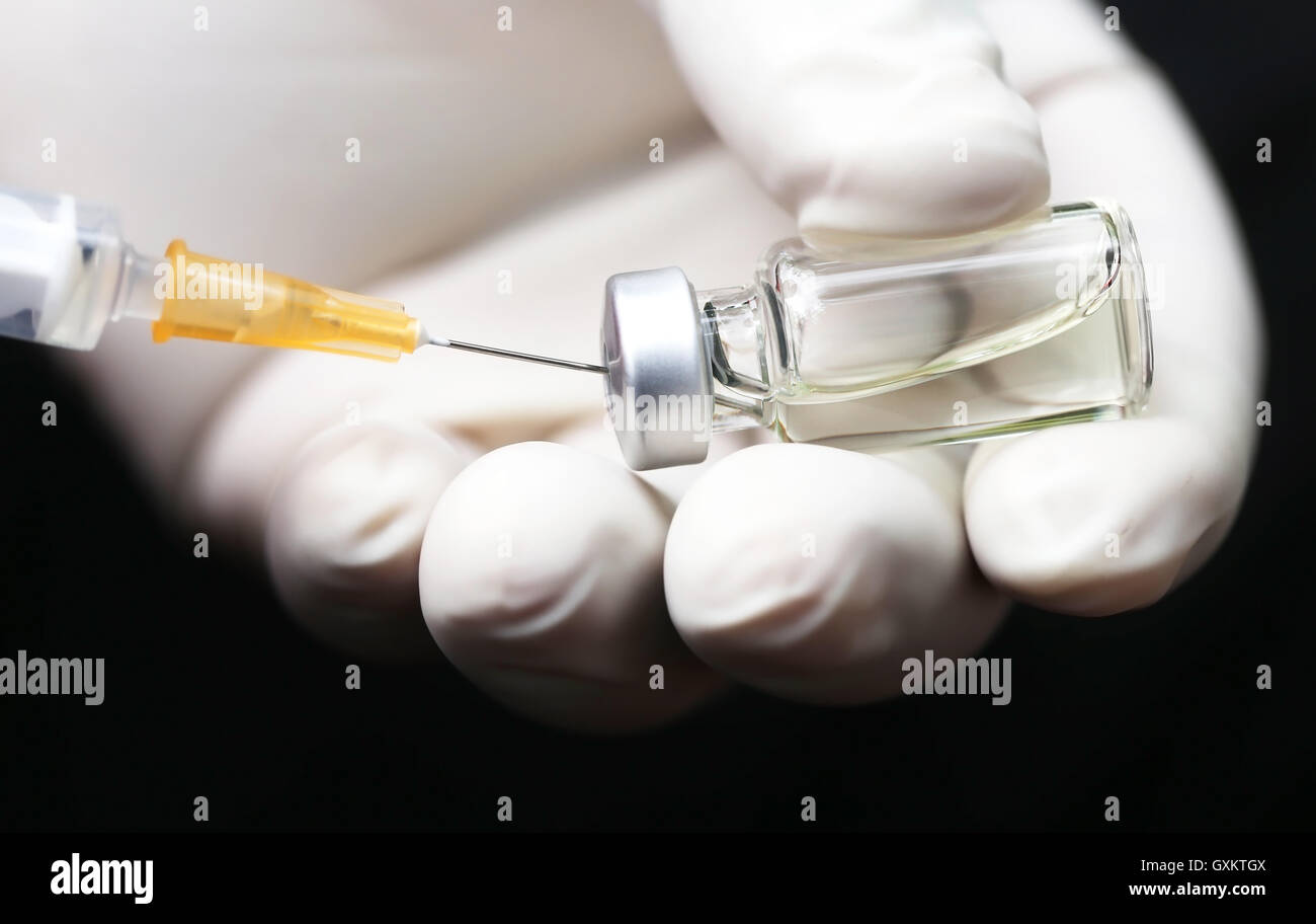 Hand holding a syringe with vial against dark background Stock Photo