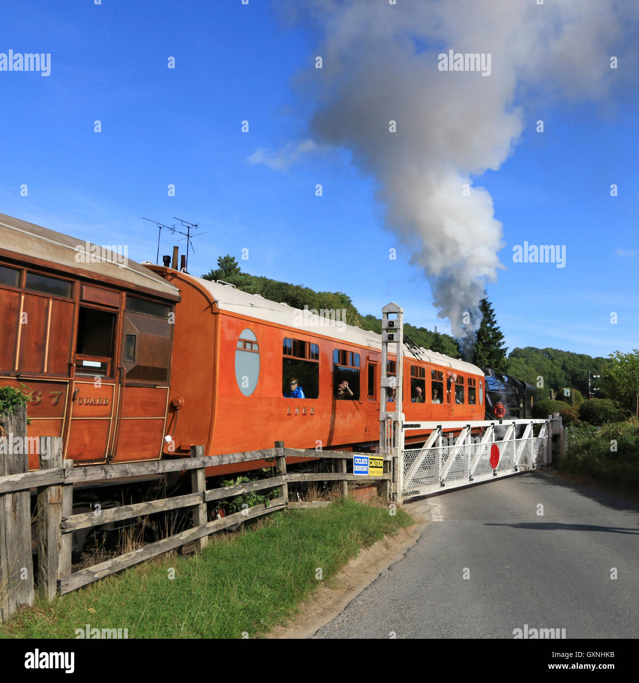 Train with steam locomotive heading to Whitby on the North York Moors Railway, passing through Newbridge level crossing. Stock Photo