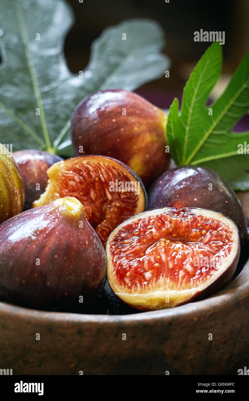 Fresh ripe black figs and fig leaves in rustic bowl Stock Photo