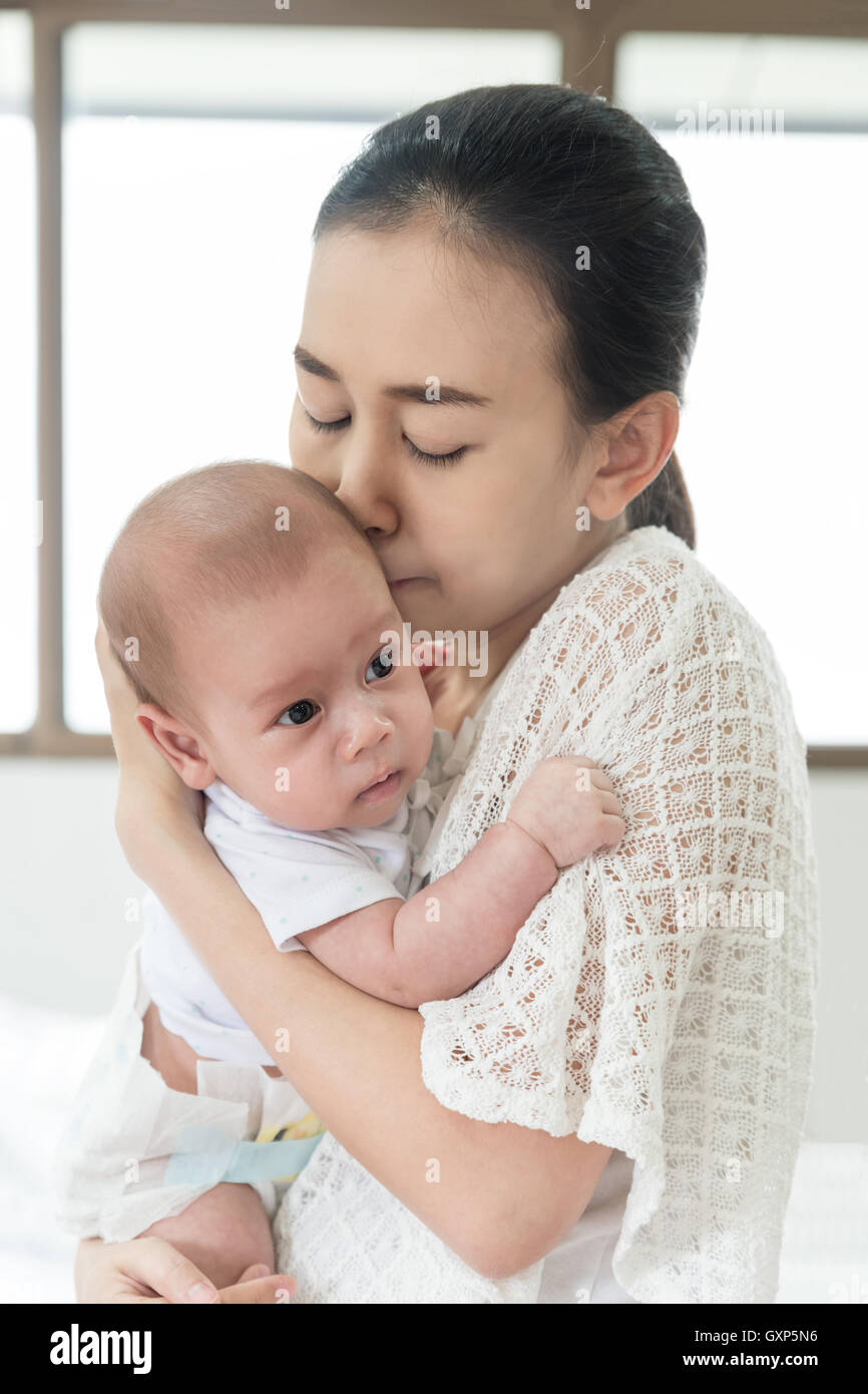 Picture of happy Asian mother kiss infant baby boy after cry. Closeup at mother and infant baby. Stock Photo