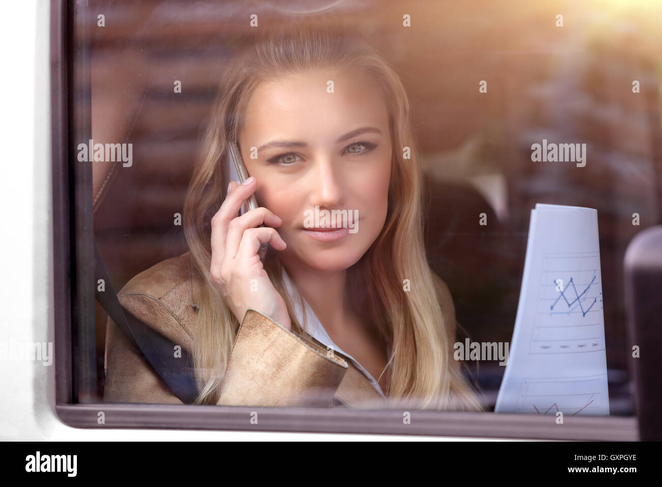 Portrait of a serious business woman in the car resolving work problems, analyzing graphics and discussing it on the phone Stock Photo