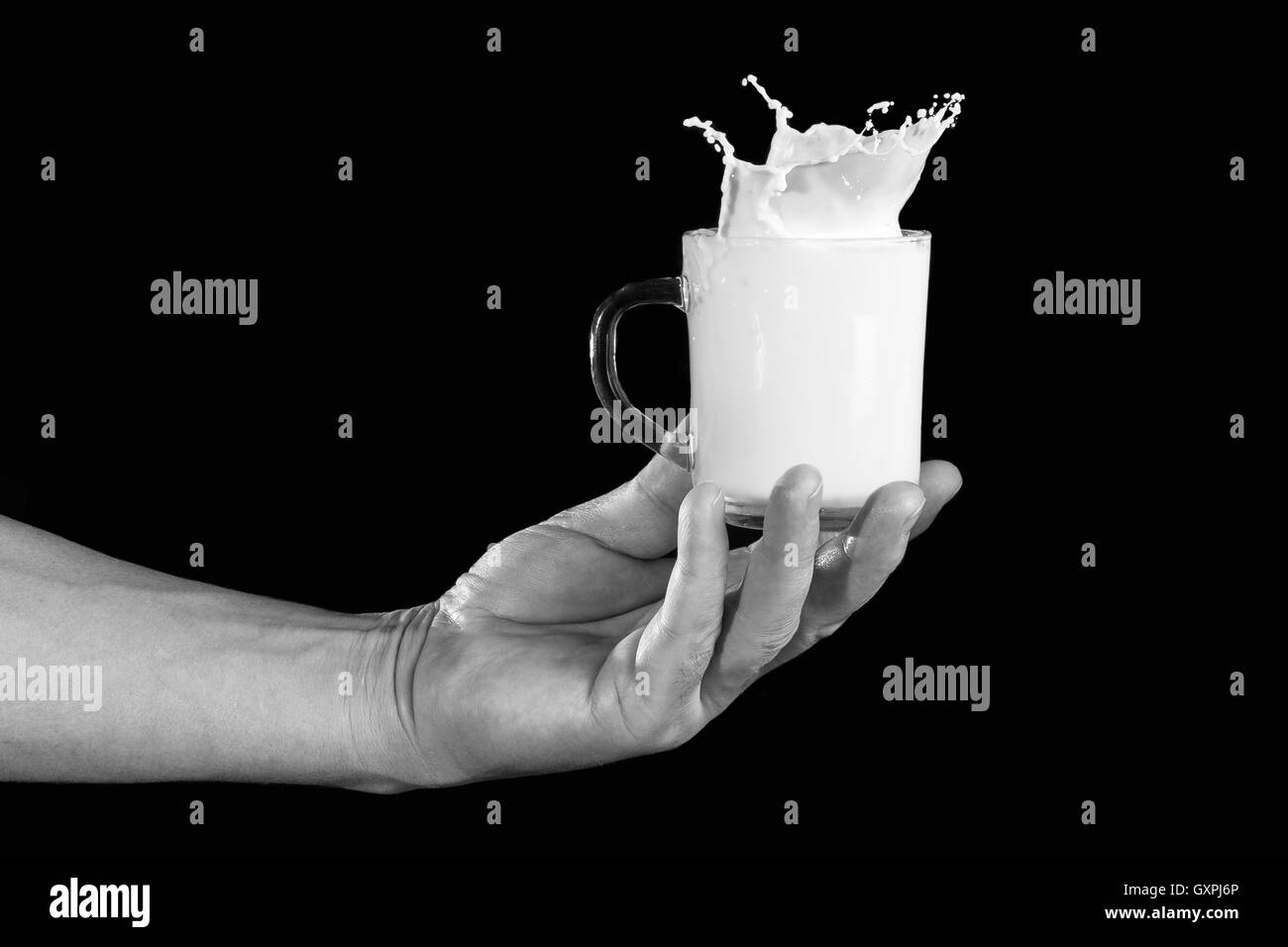 man's hand holding a cup of milk with a splash on a dark background Stock Photo