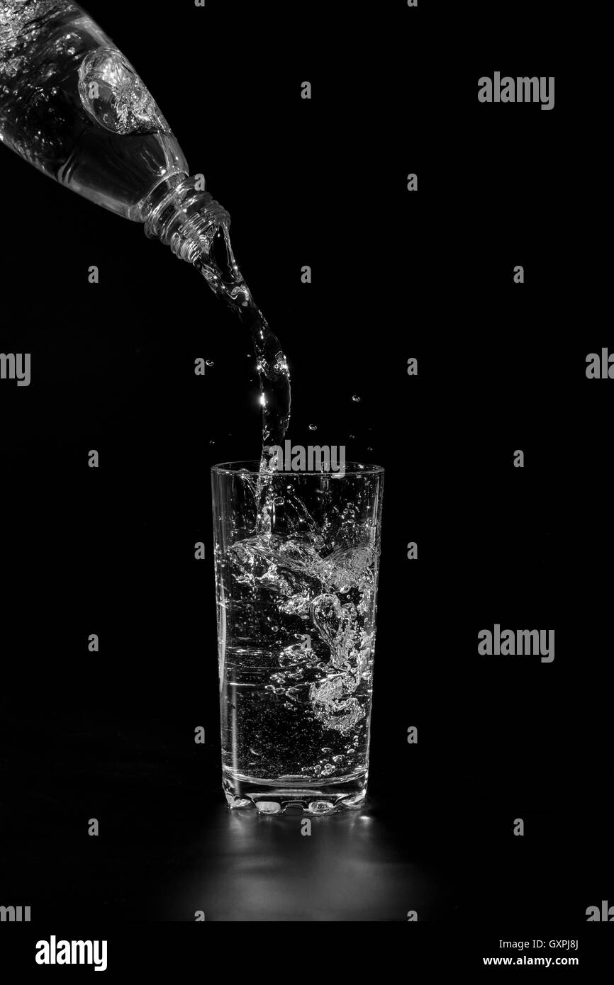 Water poured from the bottle into a transparent glass cup on a black background Stock Photo