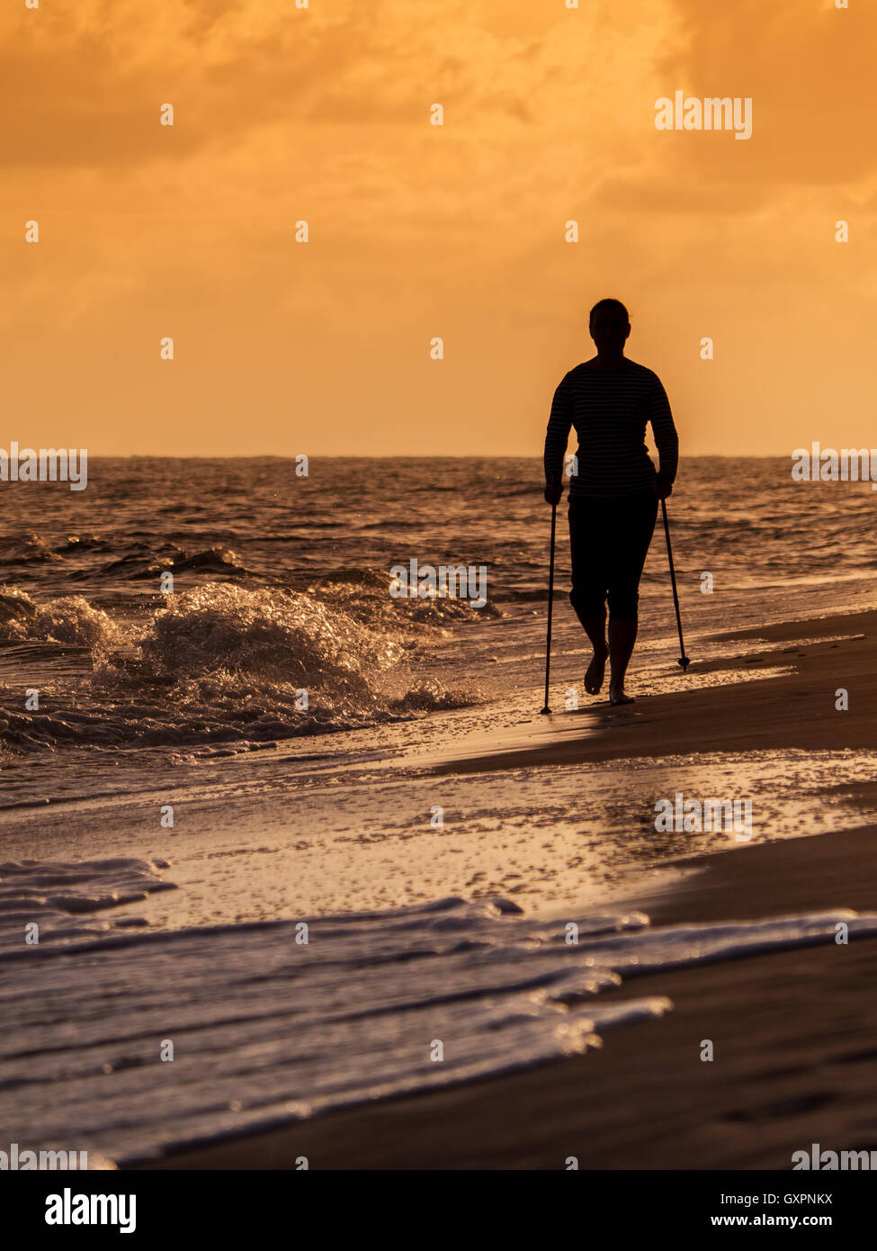 Silhouette of young woman doing Nordic walking on the beach against the sunrise sky Stock Photo