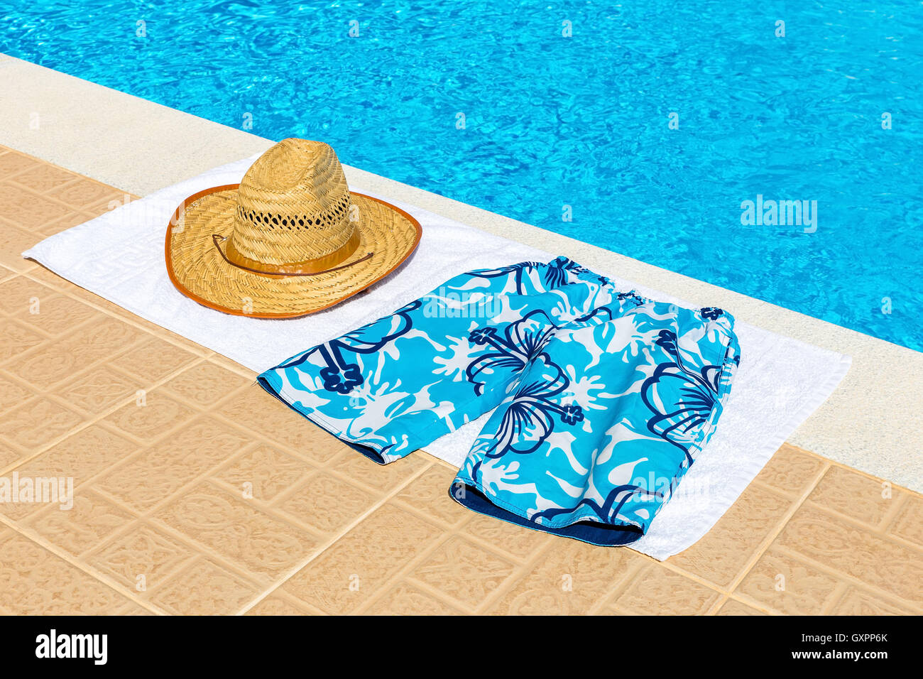 reed hat and swimming trunks on towel near blue swimming pool Stock ...
