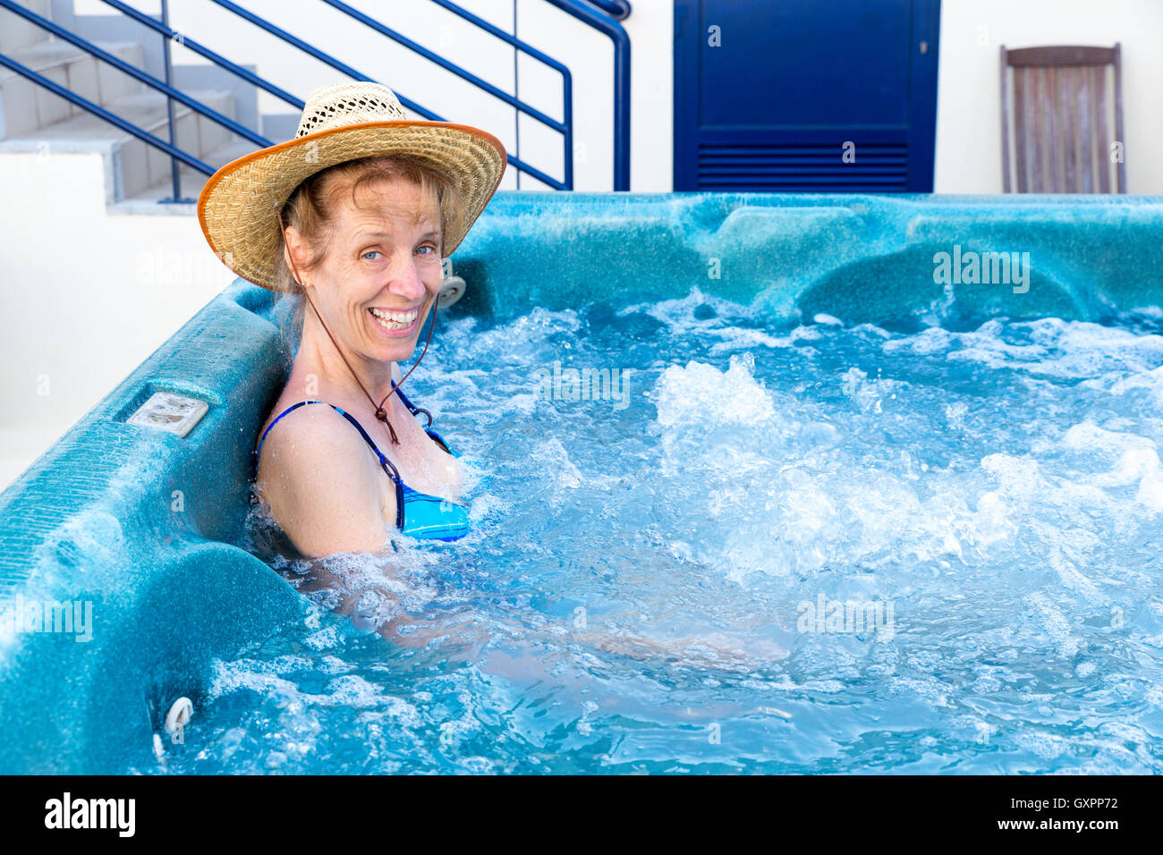 Middle aged woman with straw hat bathing in bath with bubbles Stock Photo