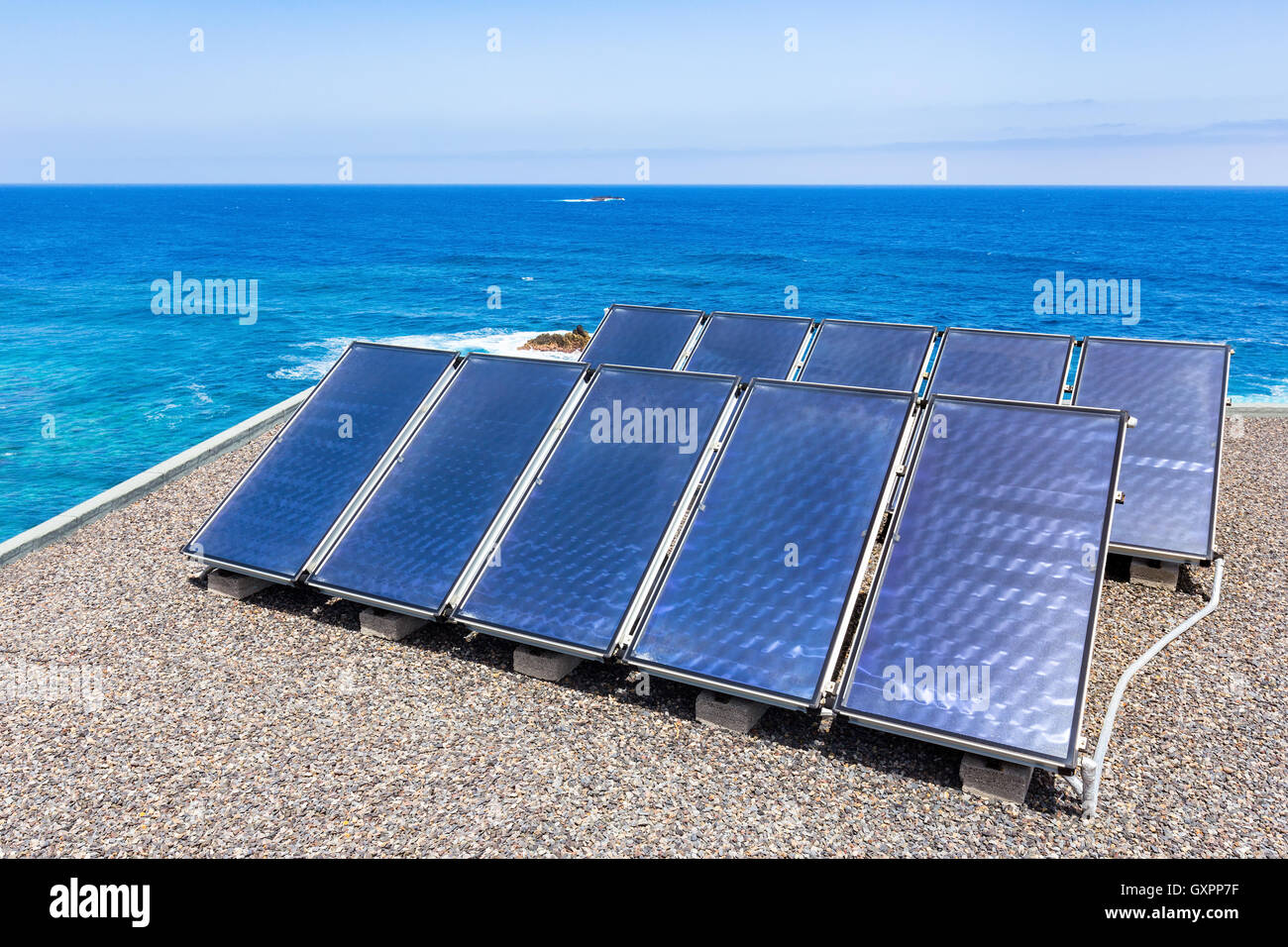 Group of blue solar panels on roof near water of ocean Stock Photo