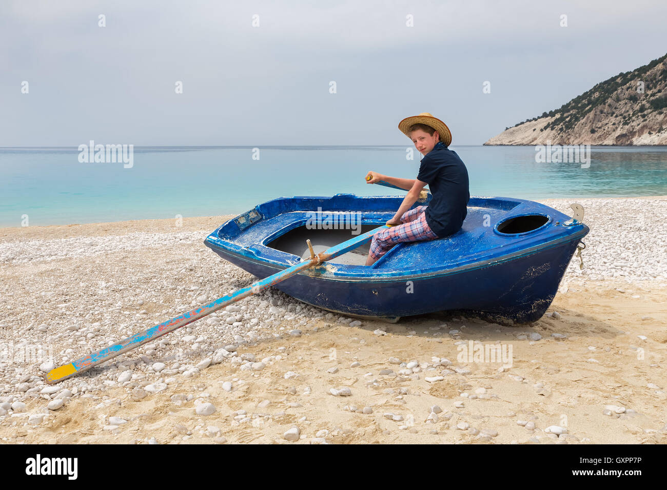 Dutch teenage boy rowing in blue boat on greek beach Stock Photo