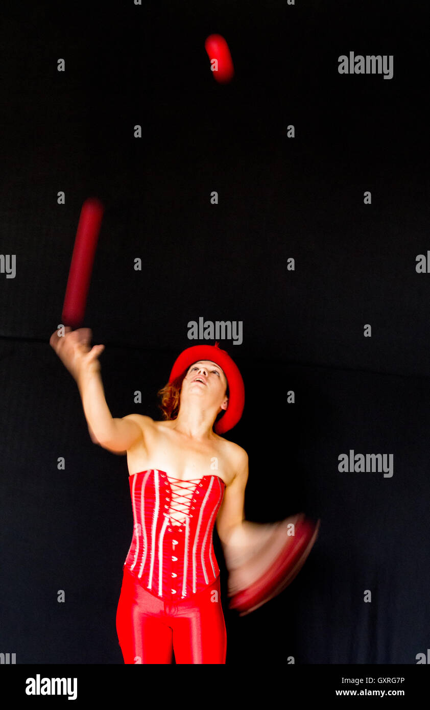 Smiling female juggler wearing a red top hat and red basque with three balls Stock Photo