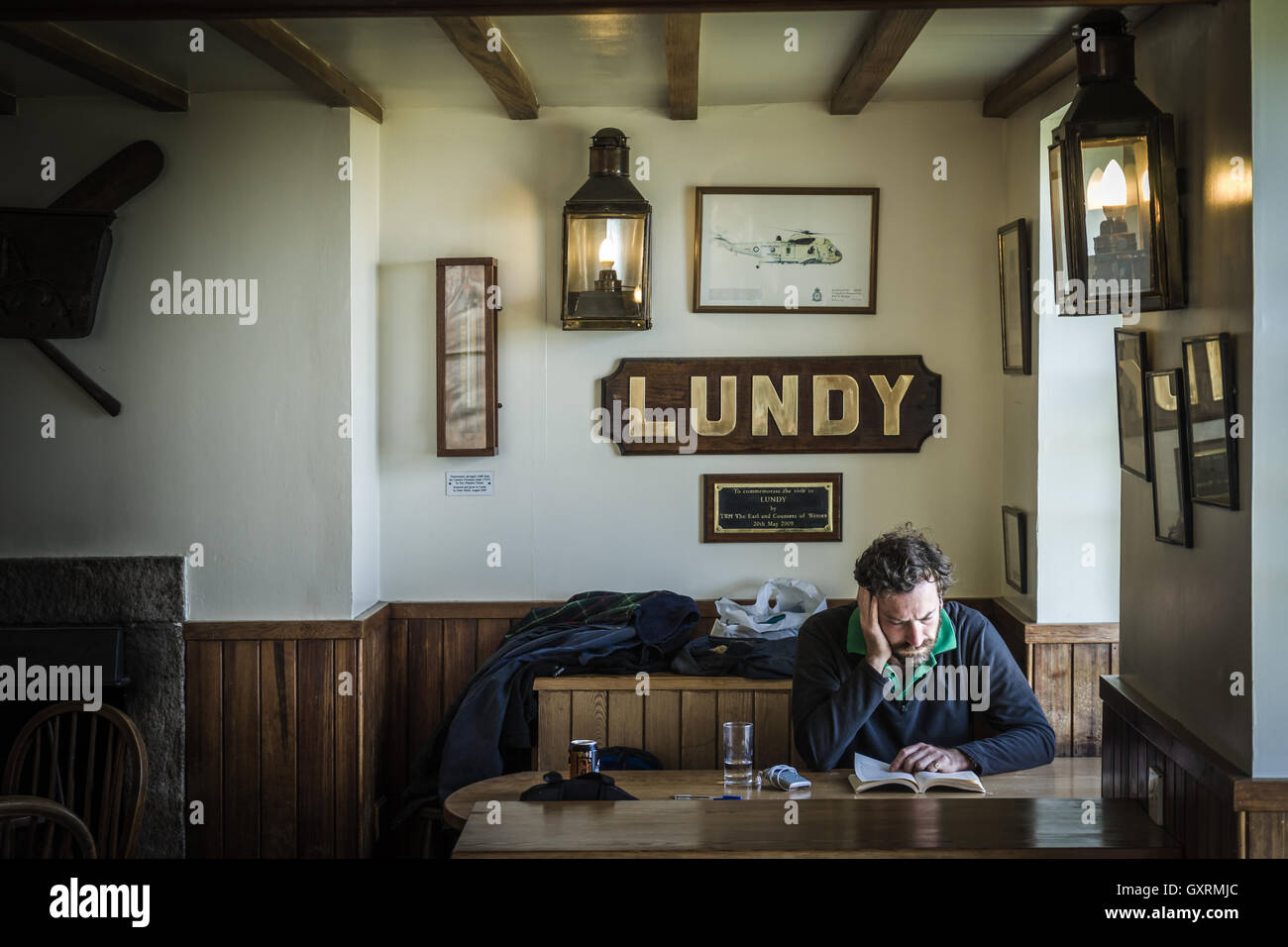 A man sits reading his book, illuminated by the light from a window, in the Marisco Tavern on Island. Stock Photo