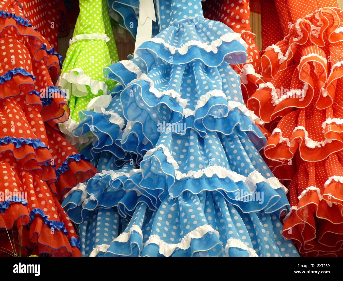 Close up of traditional blue, red, green and orange frilly flamenco dresses with white spots and lace trim hanging in a row Stock Photo