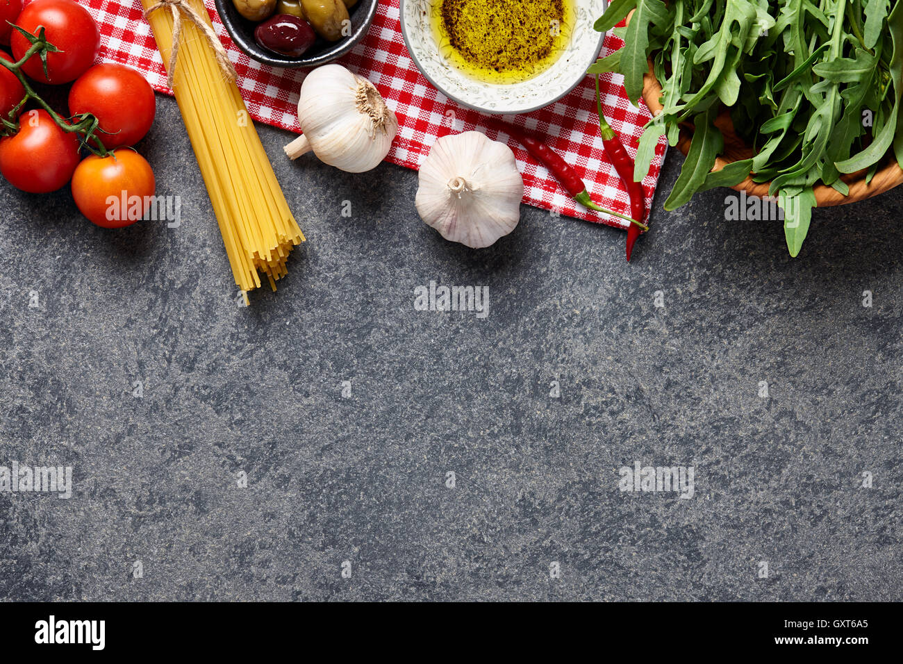 Italian food ingredients background with raw spaghetti, olives, rocket salad, garlic, olive oil and tomatoes. Stock Photo