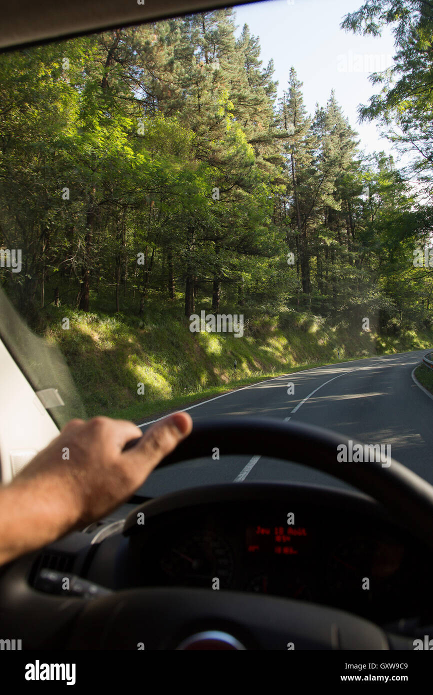 POV man driving on road through the Pyrenees in Spain, one hand visible on steering wheel Stock Photo