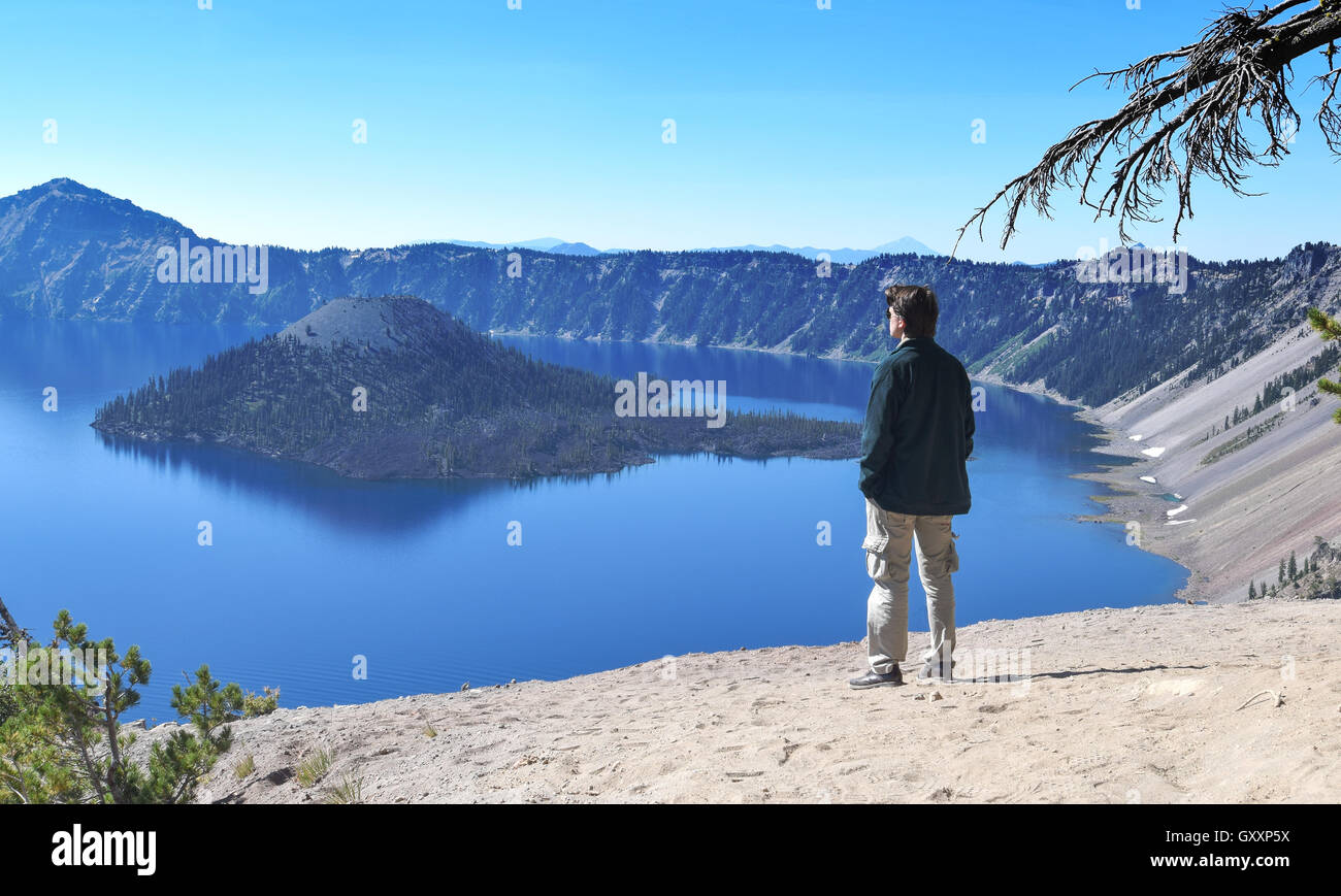 Young Caucasian man standing up looking at Crater Lake and the Wizard Island, hands in his pockets, casual dressing Stock Photo