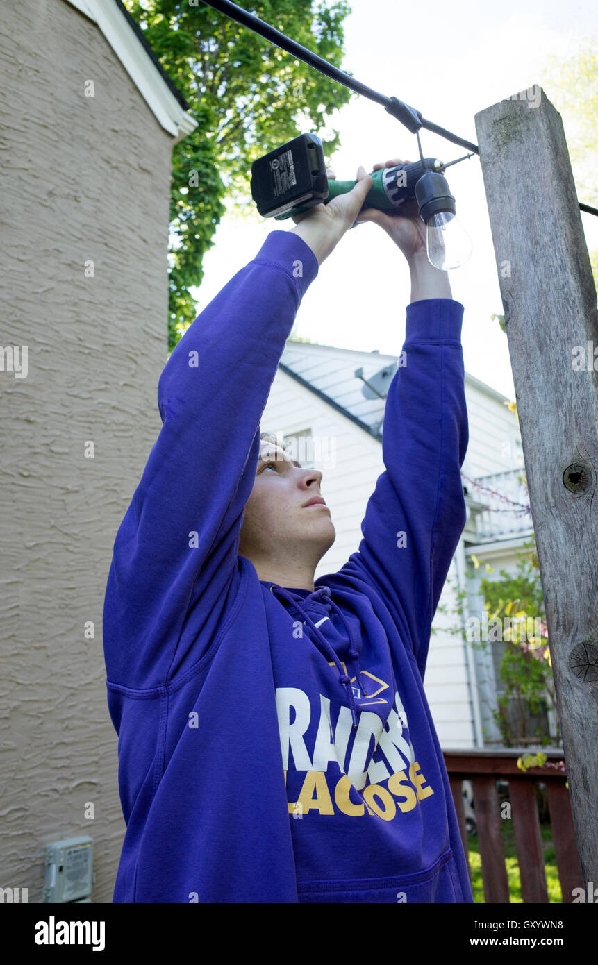 Teenager drilling hole in post to help string electrical wire. St Paul Minnesota MN USA Stock Photo