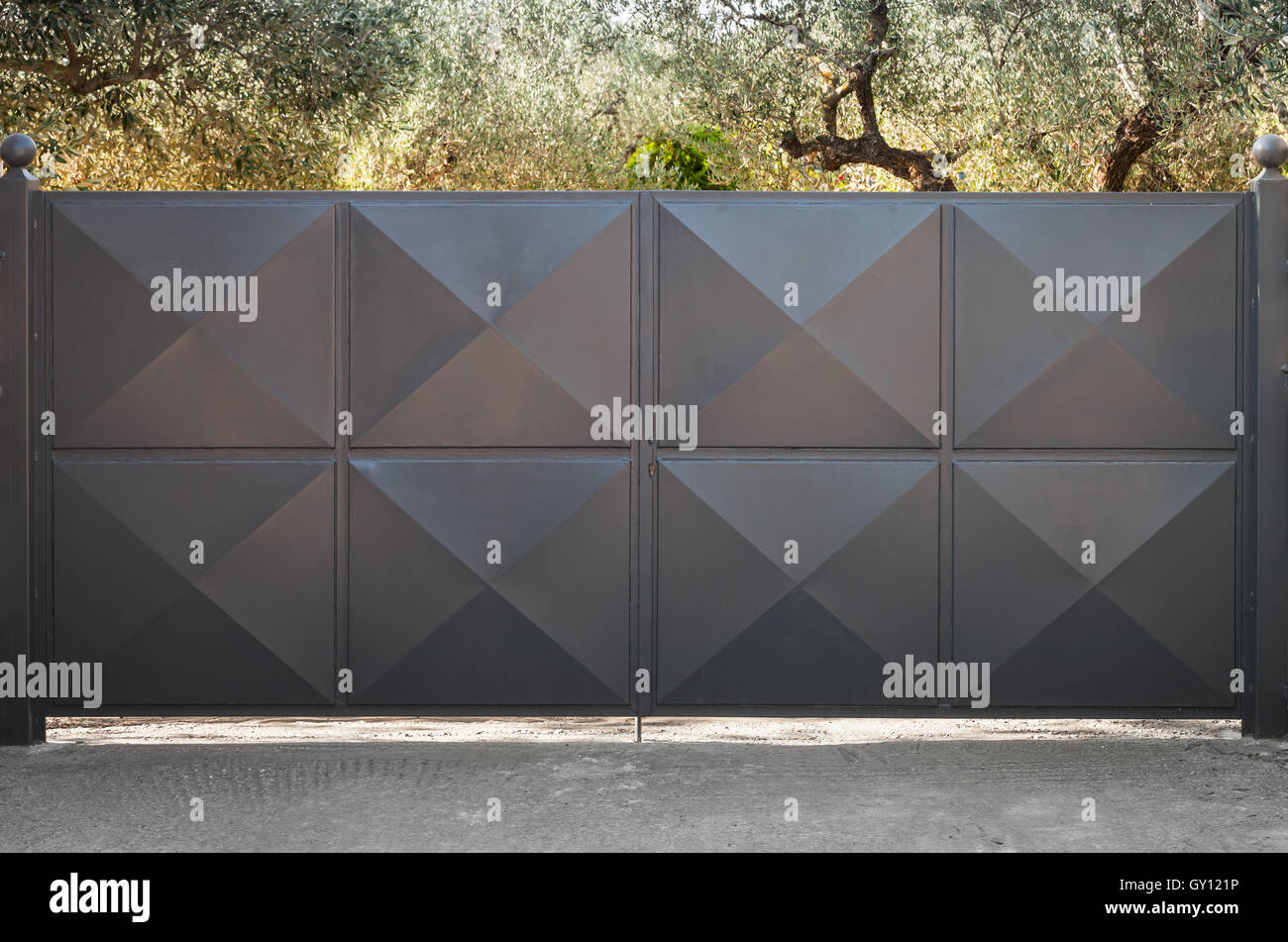 Black metal gate with square relief pattern and summer garden behind Stock Photo