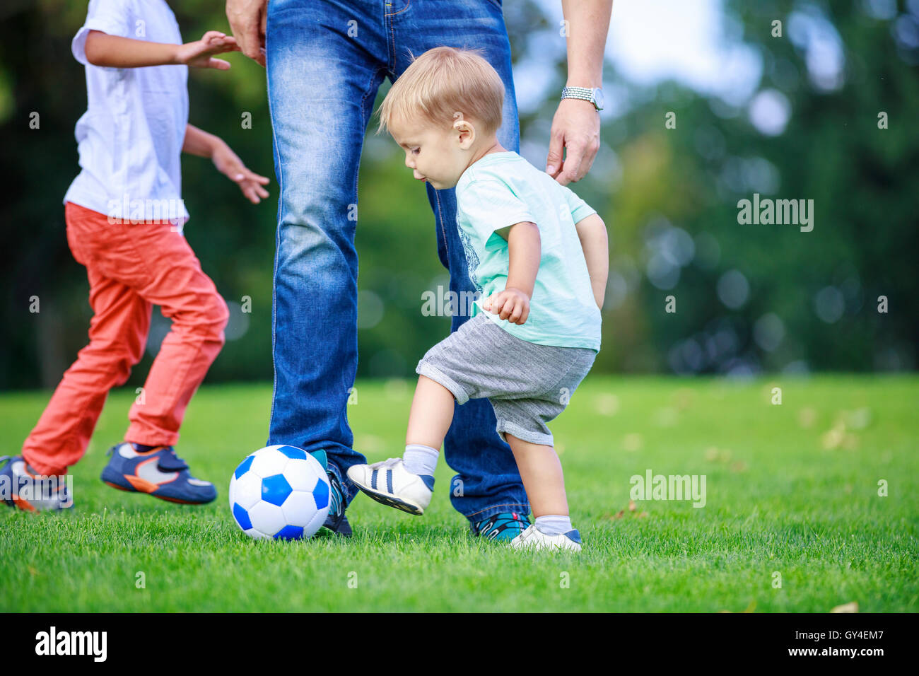 Father and sons playing football in park Stock Photo - Alamy