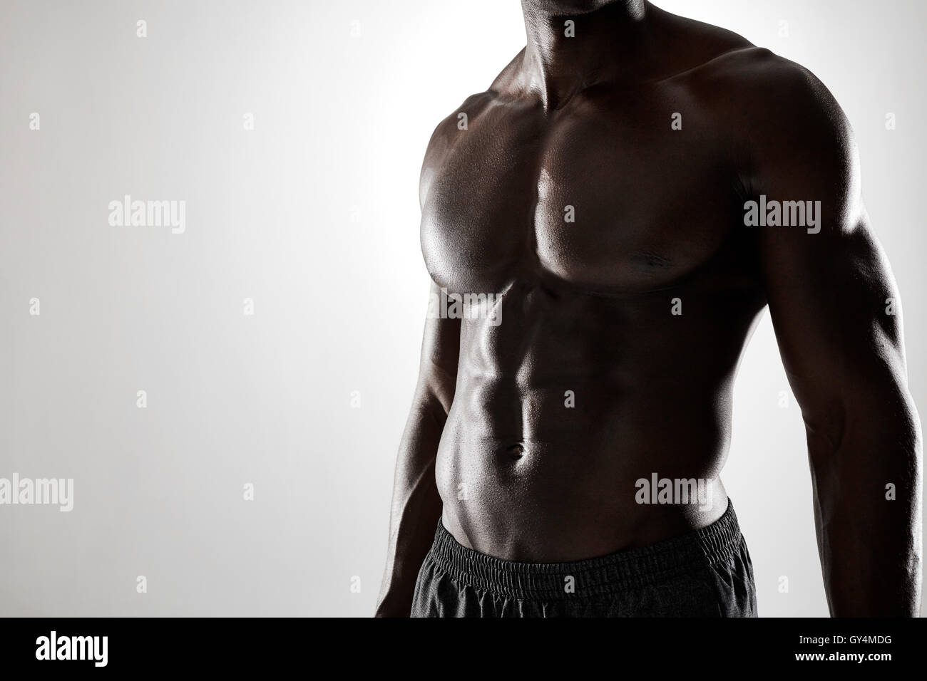 Close up shot of young african man with muscular body against grey background. Shirtless male model with muscular abs. Stock Photo