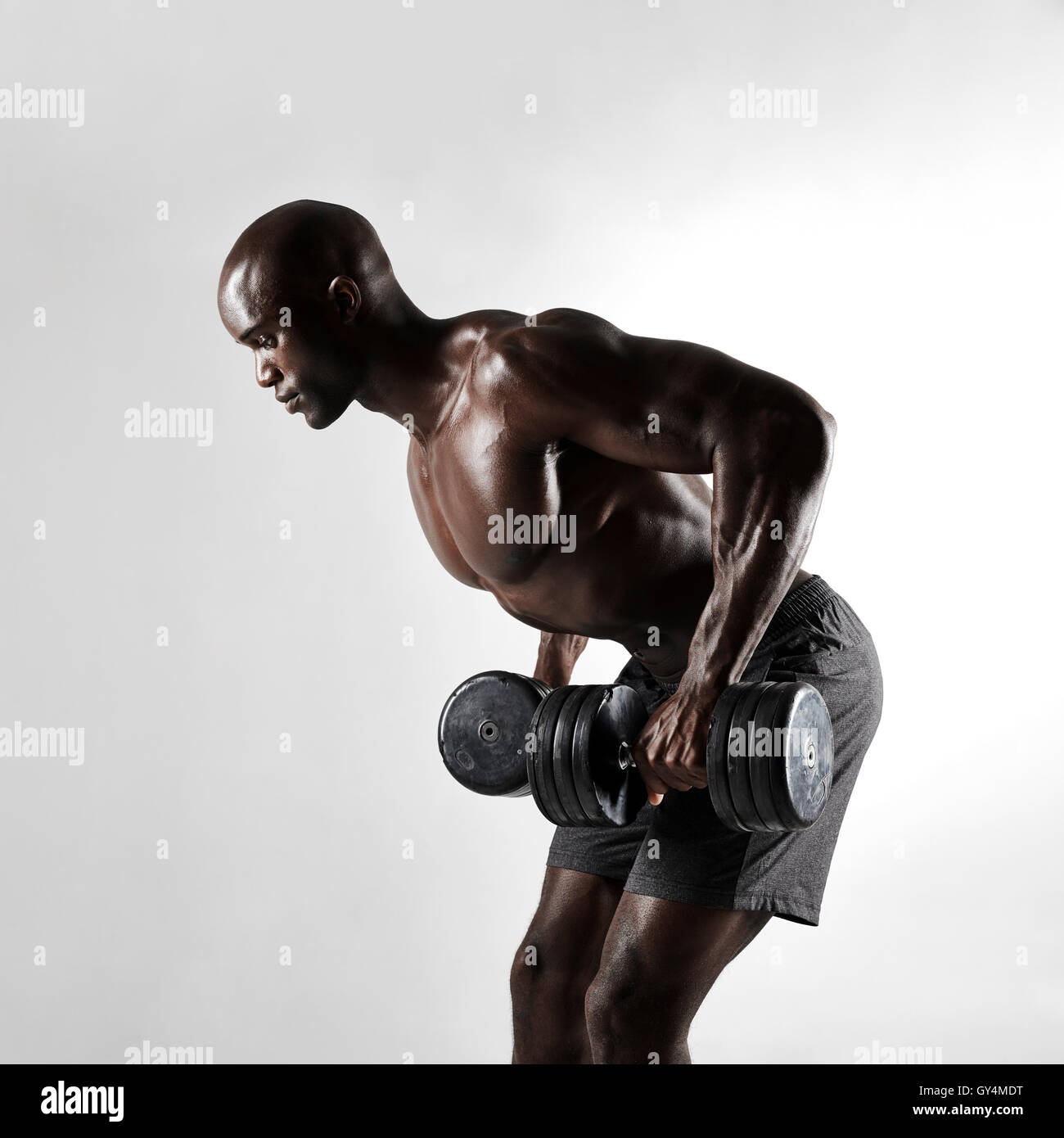 Side view shot of african bodybuilder exercising with dumbbells over grey background. Young man doing triceps exercises with hea Stock Photo