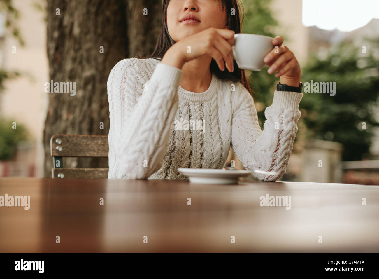 Cropped shot of young woman holding a cup of coffee at cafe. Asian female drinking coffee at cafe. Stock Photo