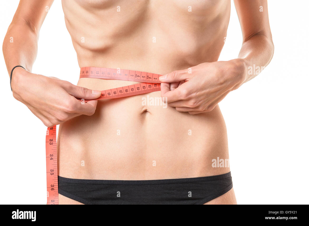 Underweight young woman measuring her waist with a tape measure with protruding ribs and hip bones conceptual of anorexia or bul Stock Photo