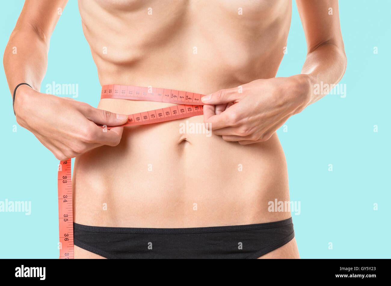 Underweight young woman measuring her waist with a tape measure with protruding ribs and hip bones conceptual of anorexia or bul Stock Photo