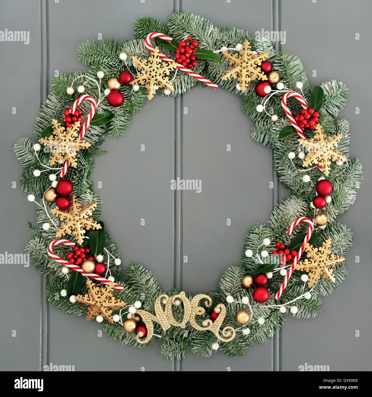 Christmas wreath with noel sign and snowflake decorations, candy canes, red and gold baubles, holly and snow covered fir. Stock Photo