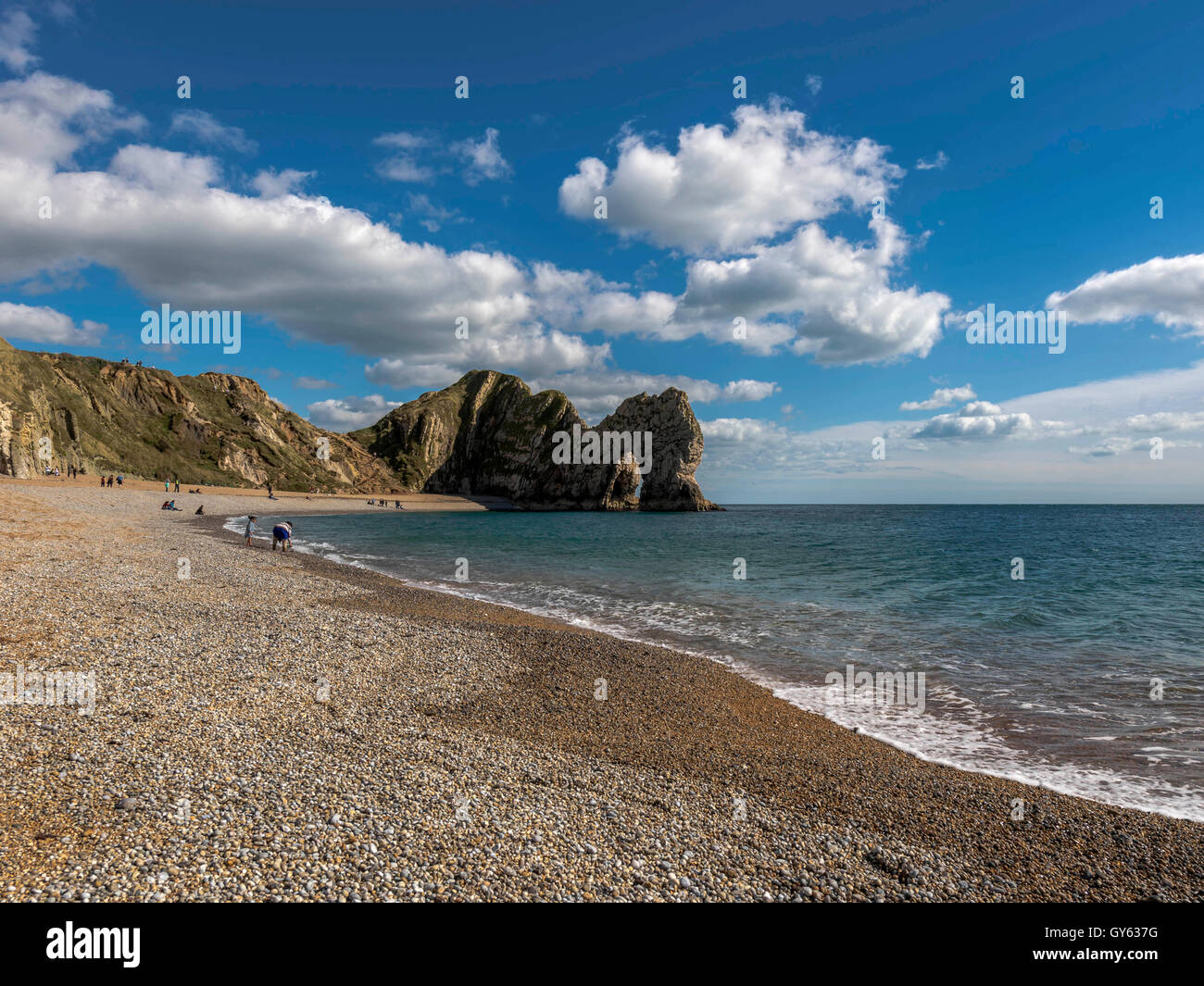 Landscape depicting the pebbled Jurassic shoreline on a fine summer day with Durdle Door in the background. Stock Photo