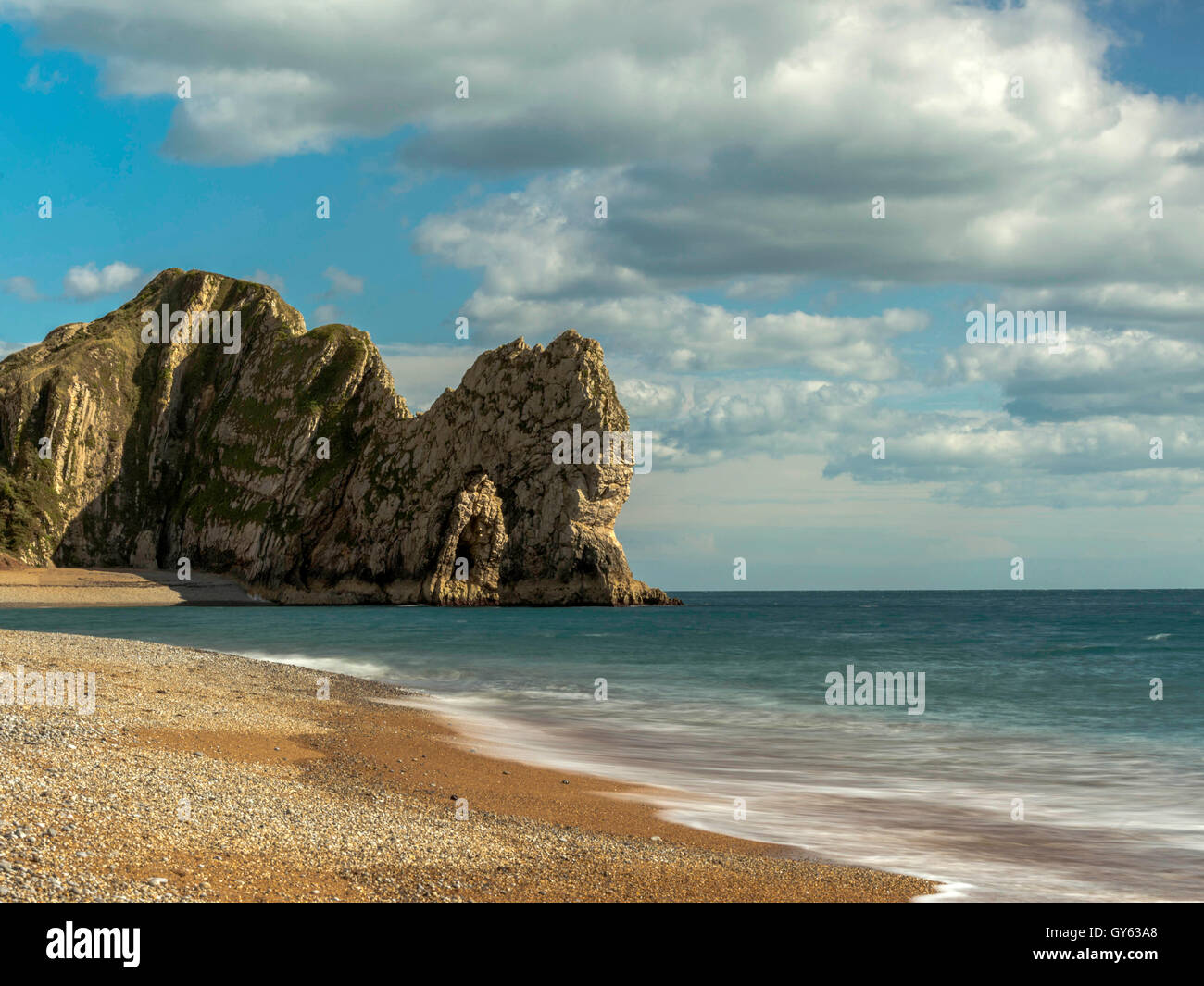 Landscape depicting the pebbled Jurassic shoreline on a fine summer day with Durdle Door headland in the background. Stock Photo