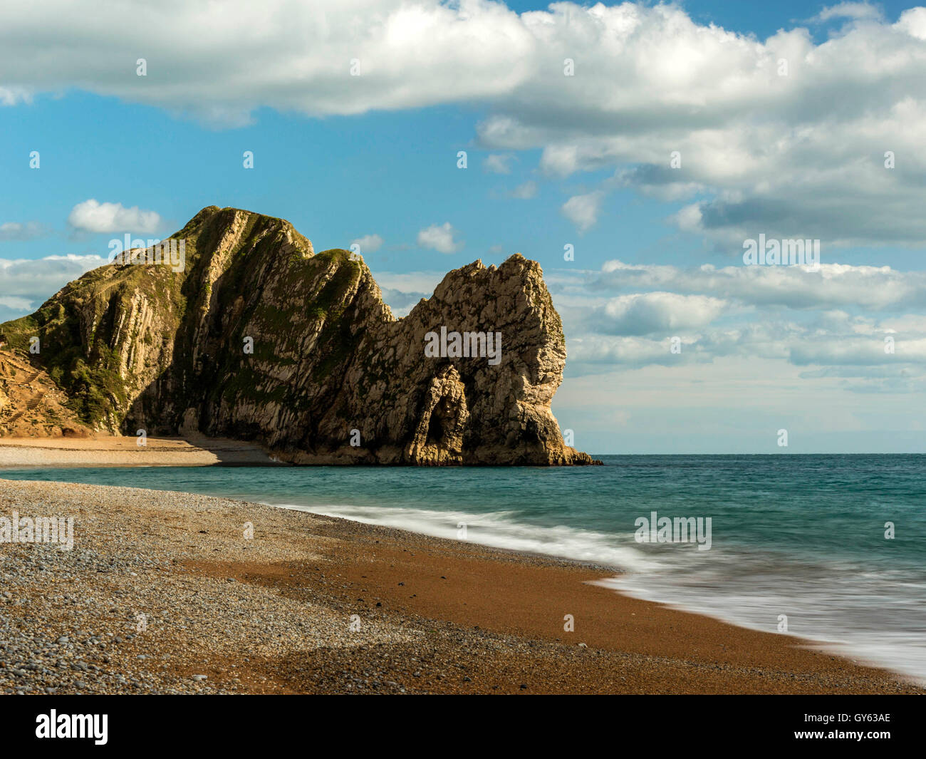 Landscape depicting the pebbled Jurassic shoreline on a fine summer day with Durdle Door headland in the background. Stock Photo