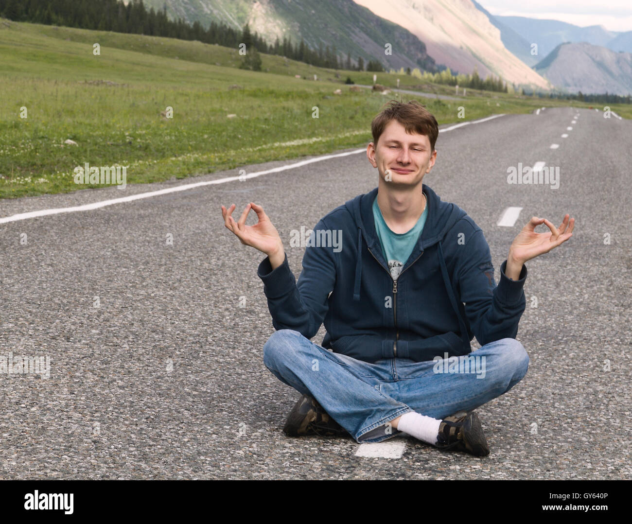 Portrait of an attractive young caucasian man (guy, male, person, model) sitting on the asphalt road among mountain landscape Stock Photo