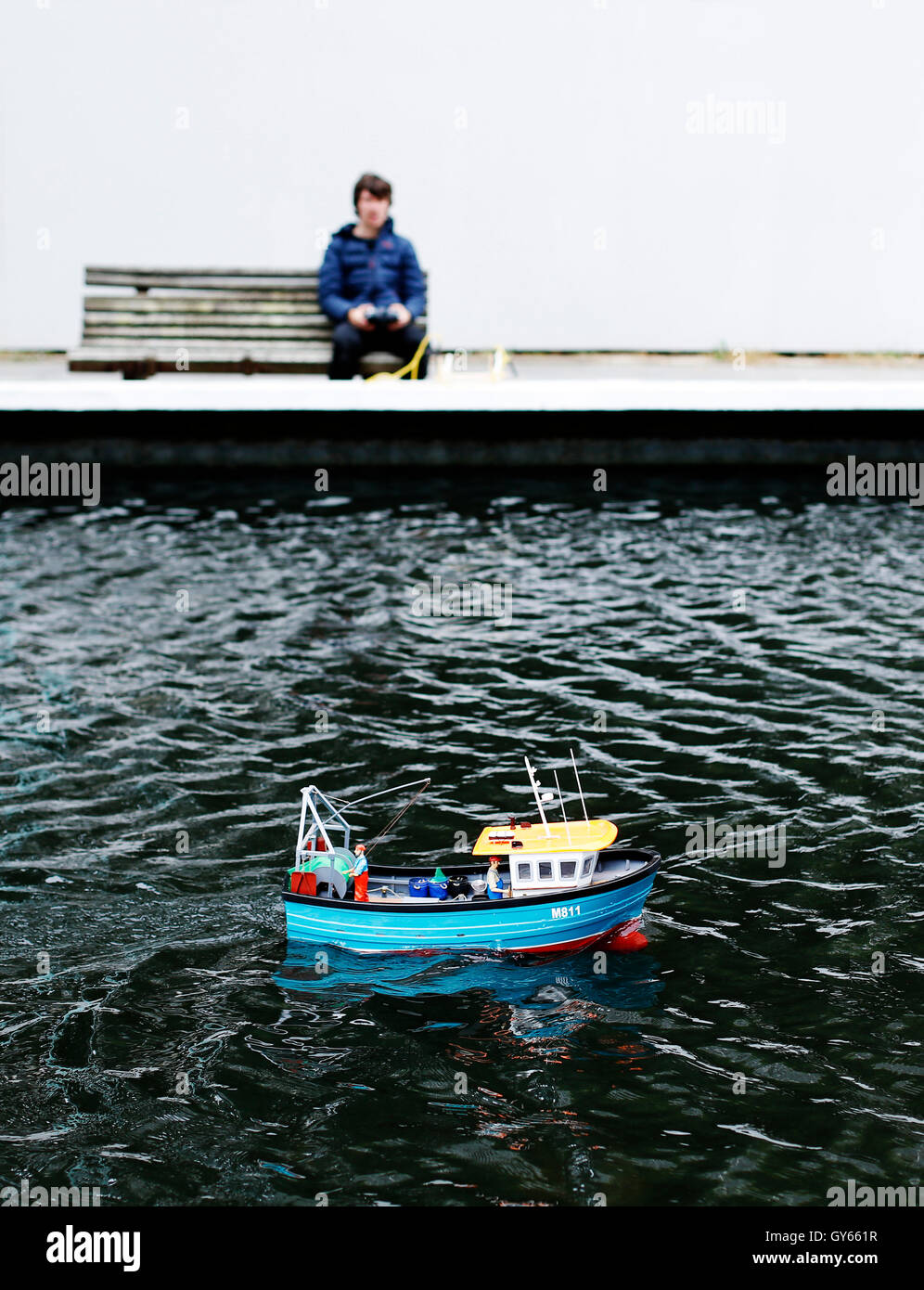 A teenage boy using a remote control boat on a pond.a Stock Photo
