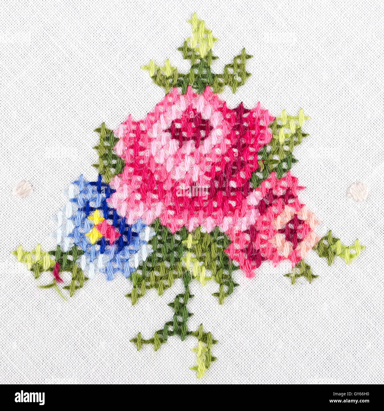 Rose motif hand embroidery on white linen tablecloth.  Multicolored cross stich decoration with yarn. Handicraft. Macro photo. Stock Photo