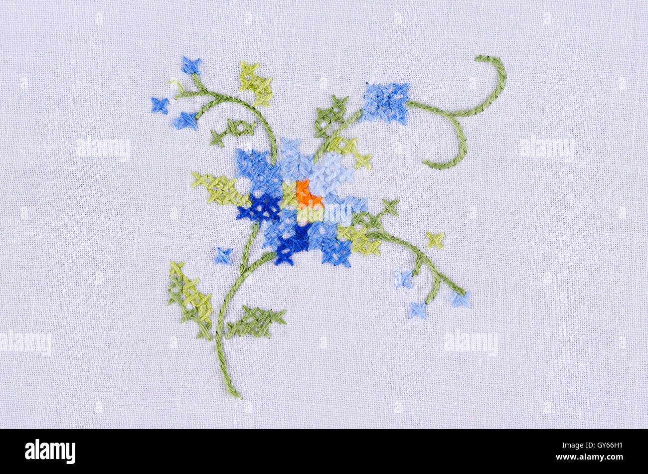 Blue flower motif hand embroidery on white linen tablecloth.  Multicolored cross stich decoration with yarn. Handicraft. Stock Photo