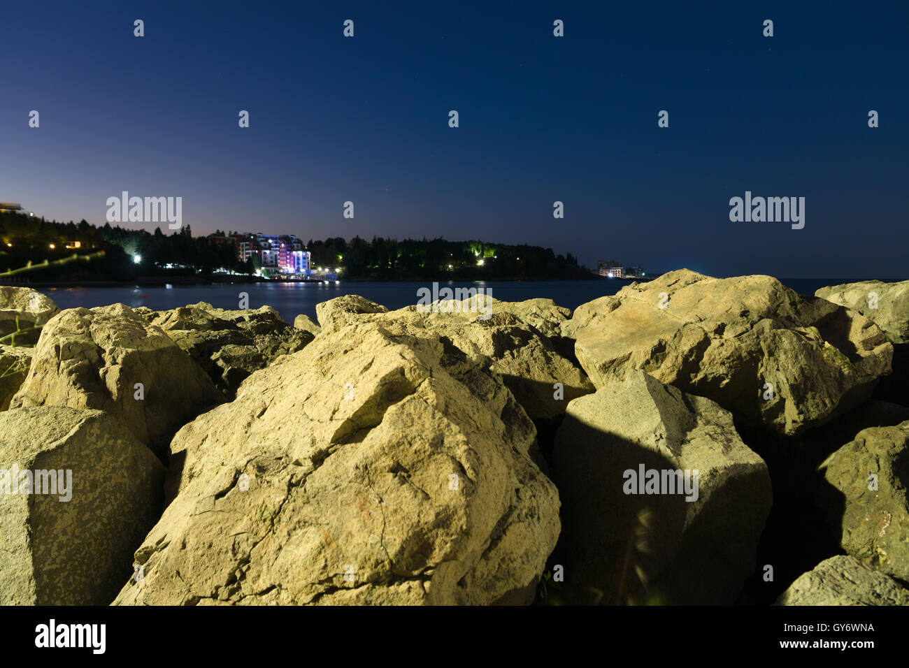 views of the glowing city lights from the shore with rocks Stock Photo