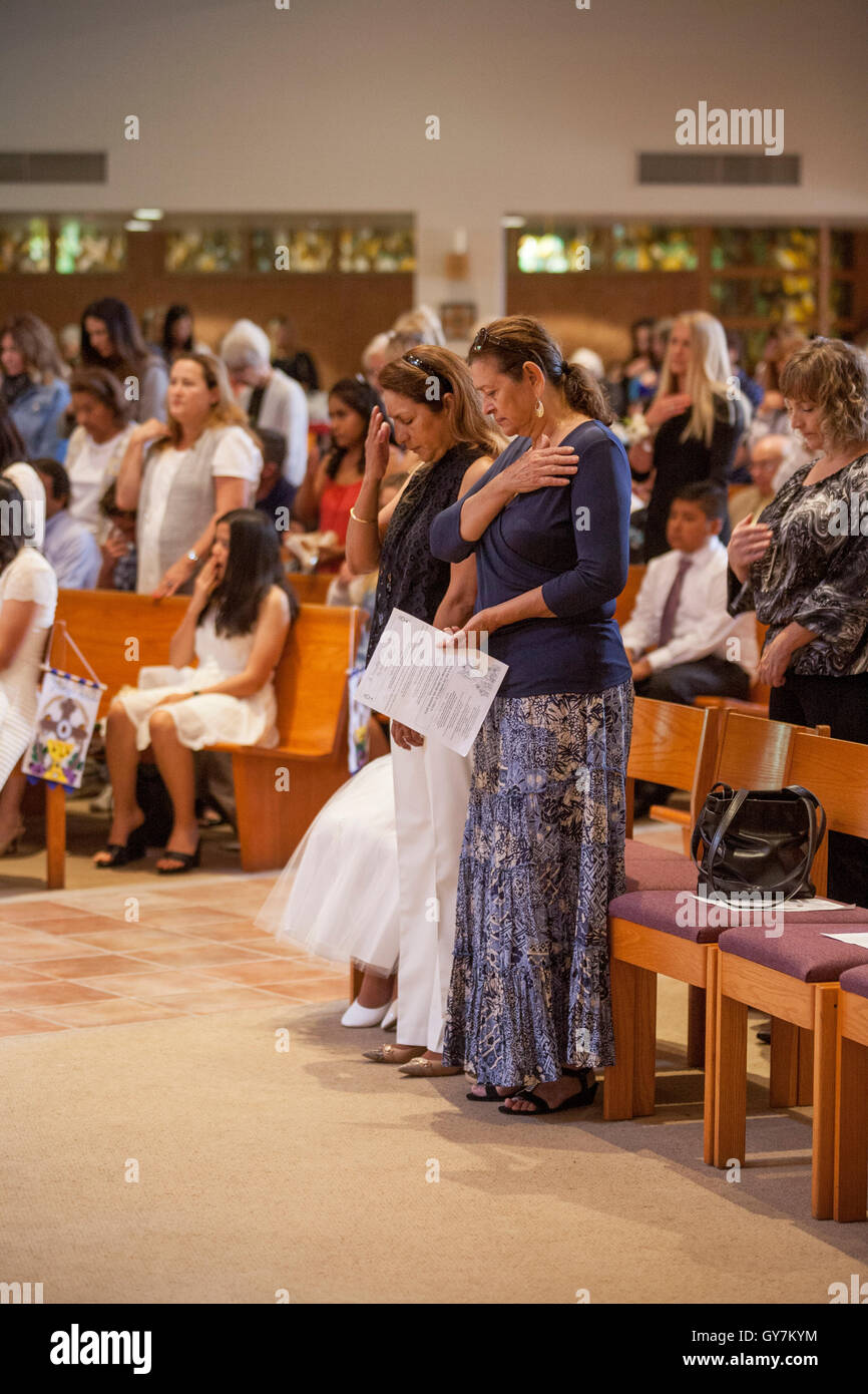 Hispanic parents cross themselves during mass as they attend First Communion ceremonies for their formally dressed children at a Laguna Niguel, CA, Catholic church. First Communion is a ceremony in some Christian traditions during which a person first rec Stock Photo