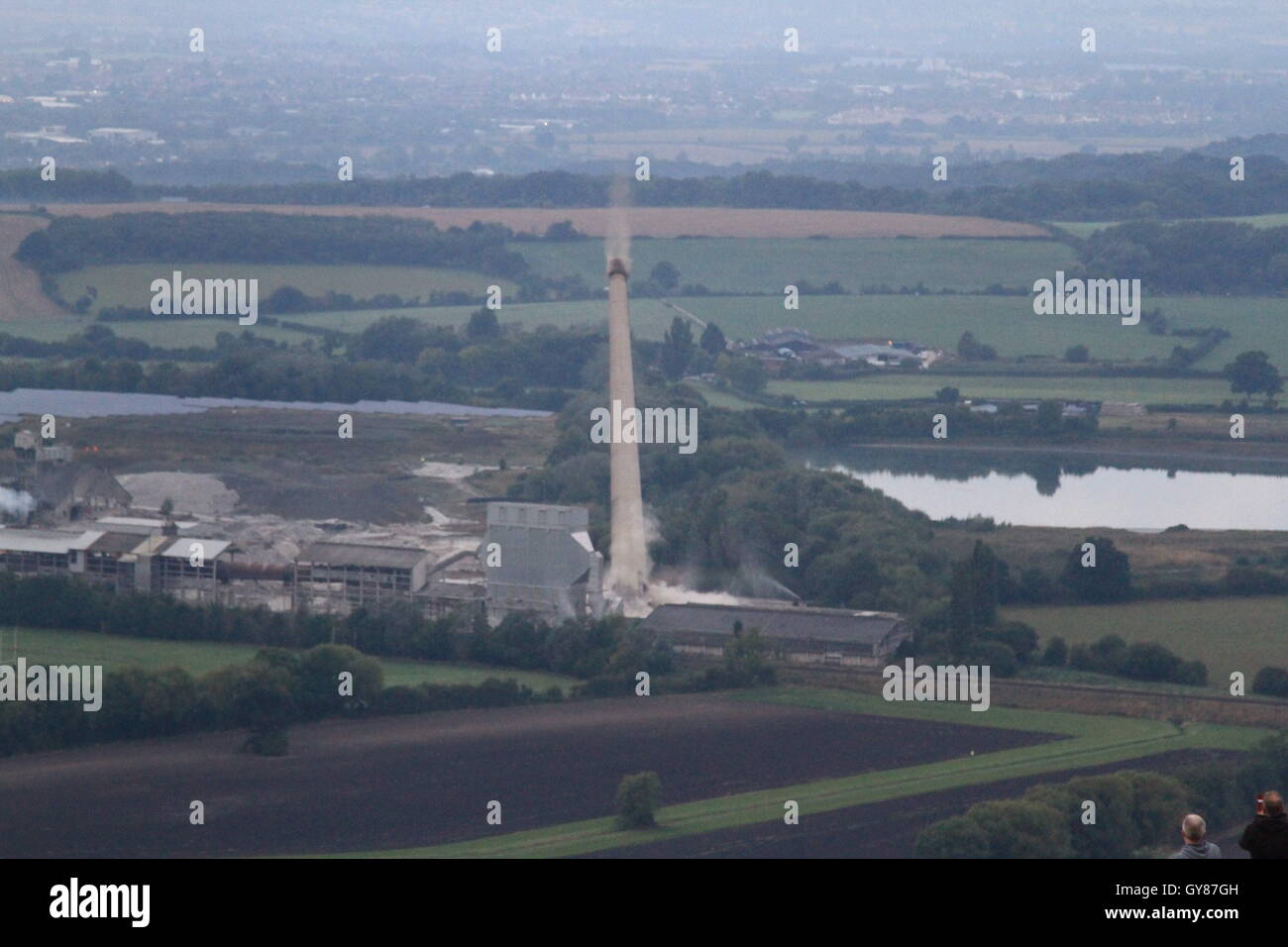 Westbury, UK, 18th Sept, 2016. The 122m high chimney of the westbury cement works, which has been a landmark of the wiltshire skyline since its construction during the 1960's is demolished using 216 charges after being mothballed in 2009.  The demolition comes after over 40 years of cement production at the site. The charges were detonated at 7am by 9 year old local schoolgirl Lilly Sargent after winning a drawing competition hosted by site owner Tarmac. Daniel Crawford / Alamy Live News Stock Photo