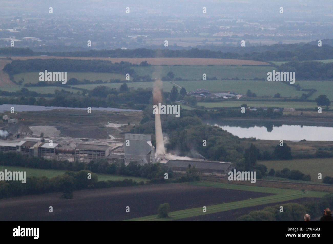 Westbury, UK, 18th Sept, 2016. The 122m high chimney of the westbury cement works, which has been a landmark of the wiltshire skyline since its construction during the 1960's is demolished using 216 charges after being mothballed in 2009.  The demolition comes after over 40 years of cement production at the site. The charges were detonated at 7am by 9 year old local schoolgirl Lilly Sargent after winning a drawing competition hosted by site owner Tarmac. Daniel Crawford / Alamy Live News Stock Photo