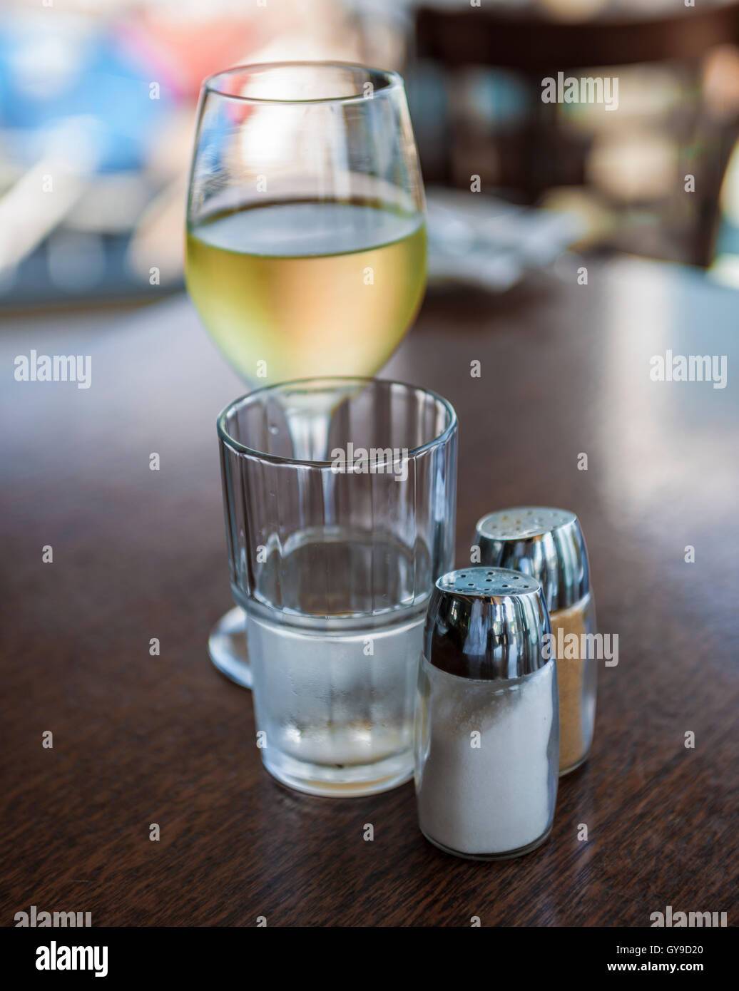 Glass of white wine, glass of water, salt and pepper shakers on wooden table at cafe Stock Photo