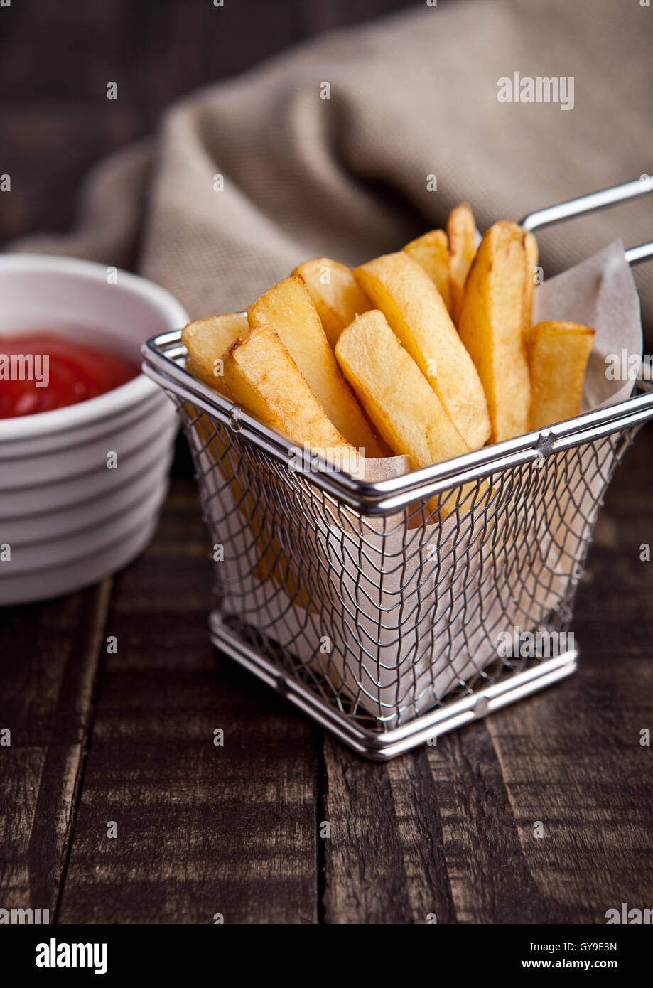 Fried french fries chips in fryer with ketchup on wood Stock Photo