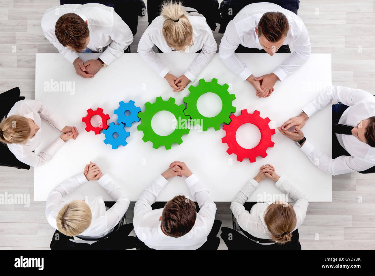 Business team sitting around the table with cogs, teamwork concept Stock Photo