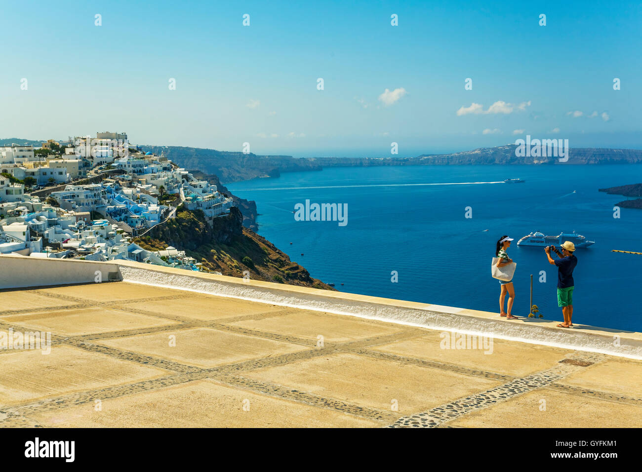 Young and actractive couple of Asiatic tourist taking pictures on a terrace in Thira, Fira, Santorini, Greece Stock Photo