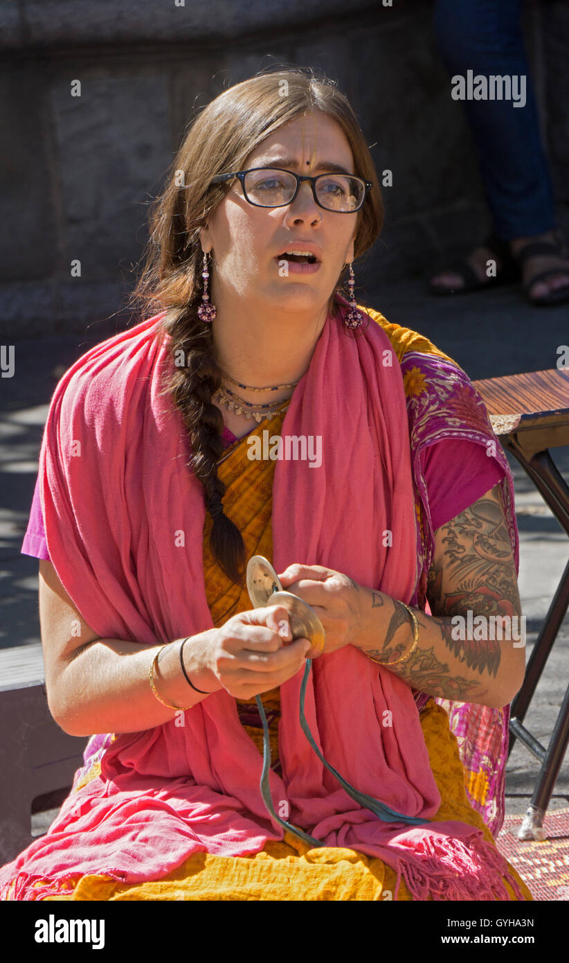 A Hare Krishna devotee with several tattoos playing the cymbals & chanting in Union Square Park in Manhattan, New York City Stock Photo