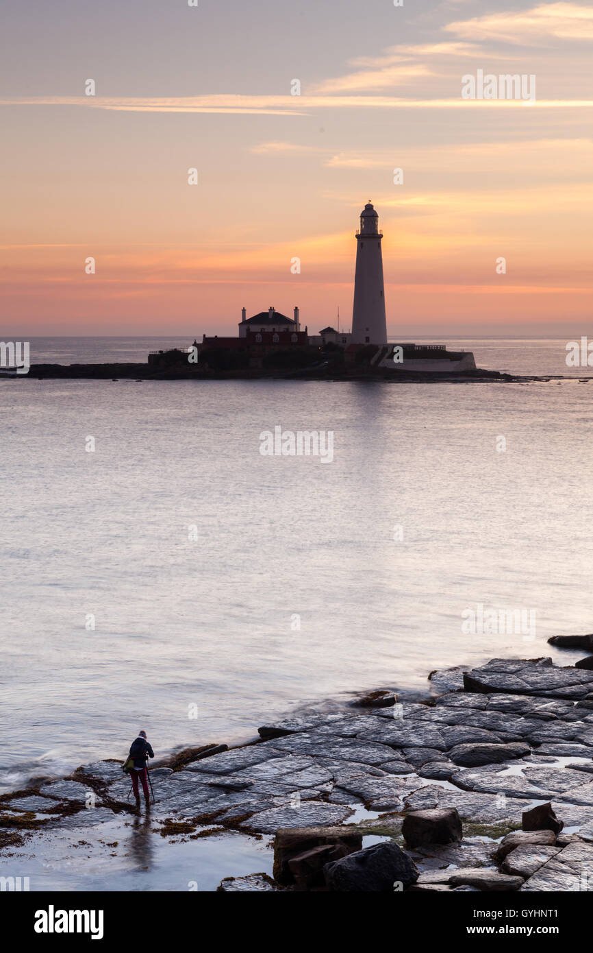 St Mary's Lighthouse at sunrise with a photographer taking photographs on the rocks, Whitley Bay, North East England Stock Photo