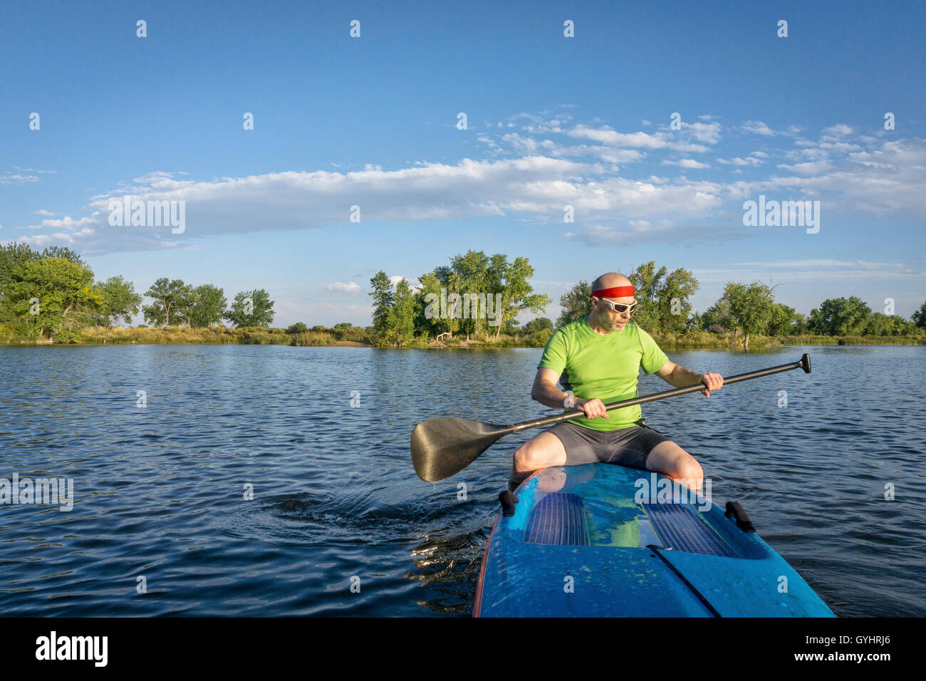 muscular, senior male paddler sitting on a stand up paddleboard on a