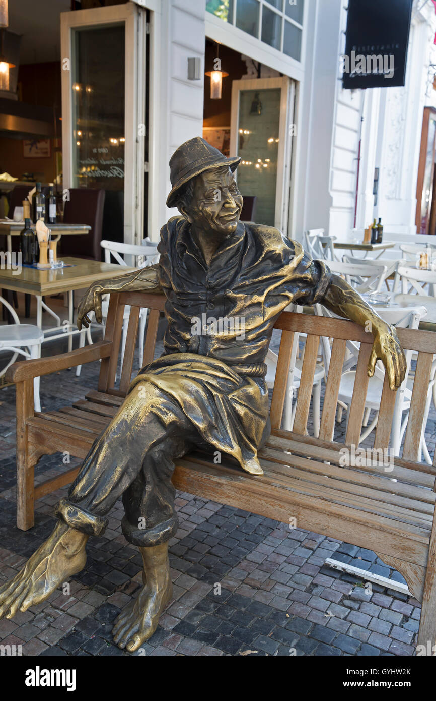Bronze statue of a man sitting on a wooden bench outside a restaurant