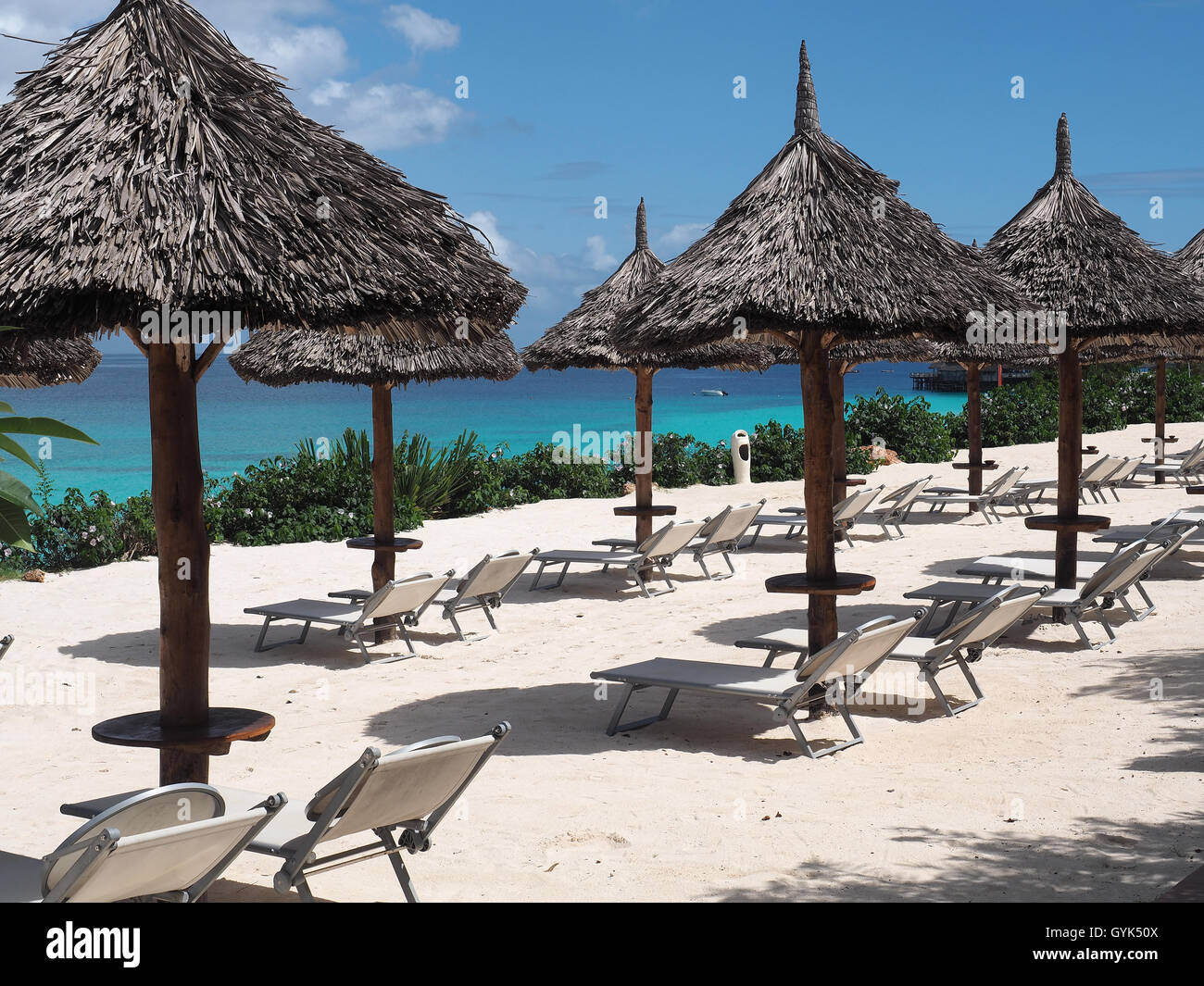 View along a row of thatched sun shade umbrellas on a white sandy beach against a bright blue sky Stock Photo