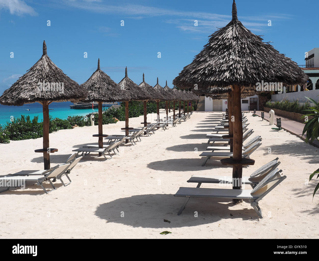 View along a row of thatched sun shade umbrellas on a white sandy beach against a bright blue sky Stock Photo