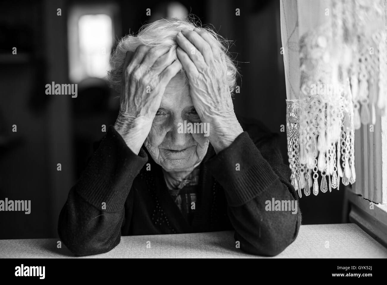 An elderly woman sitting at the table in a depressed state, black and white photo. Stock Photo