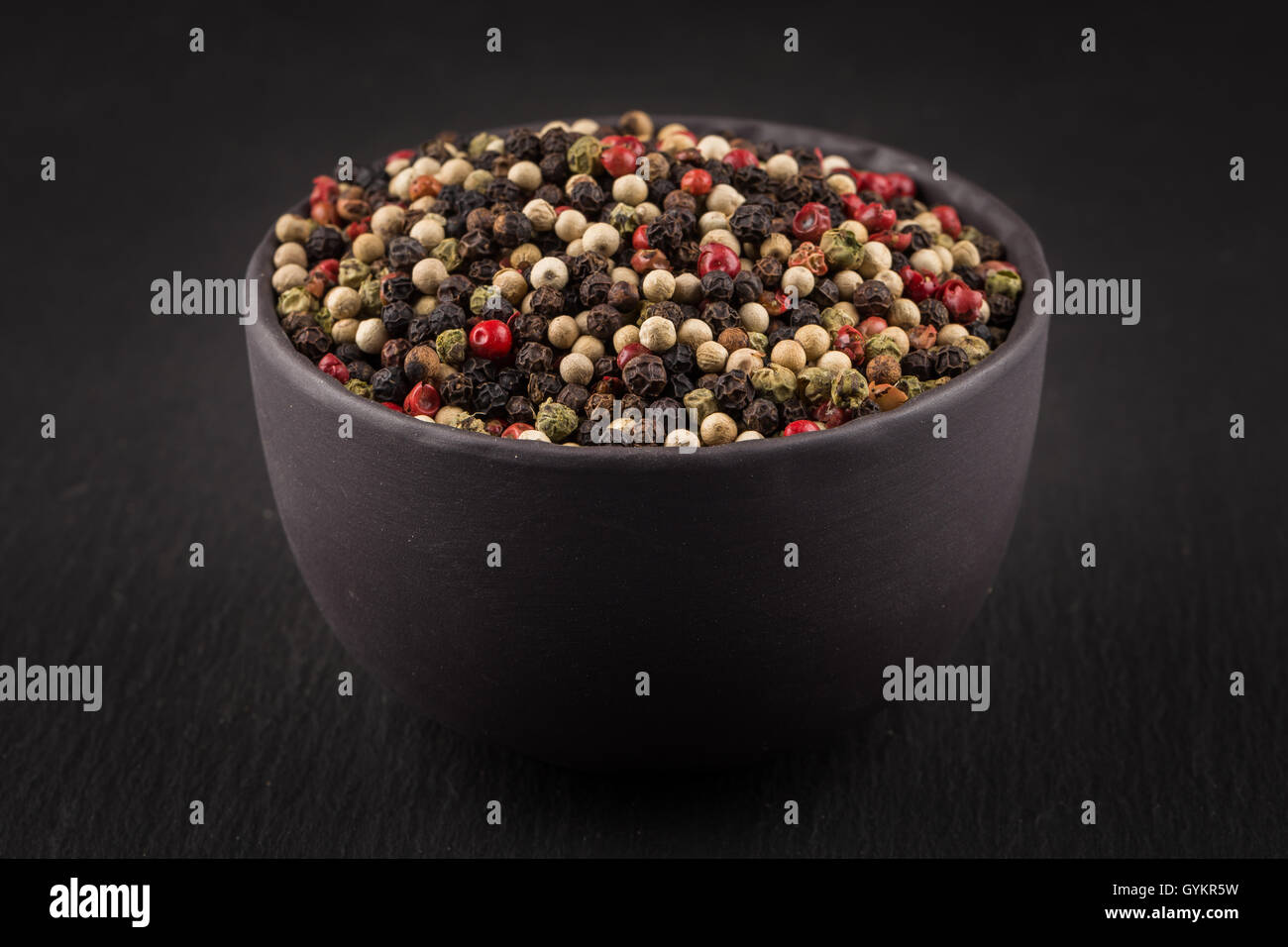 bowl of various pepper peppercorns seeds mix on dark stone Stock Photo